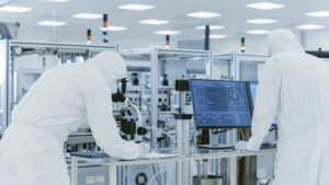 In Laboratory Scientists in Protective Clothes Doing Research, Using Microscope and Entering Data into Personal Computer. Modern Manufactory Producing Semiconductors and Pharmaceutical Items.